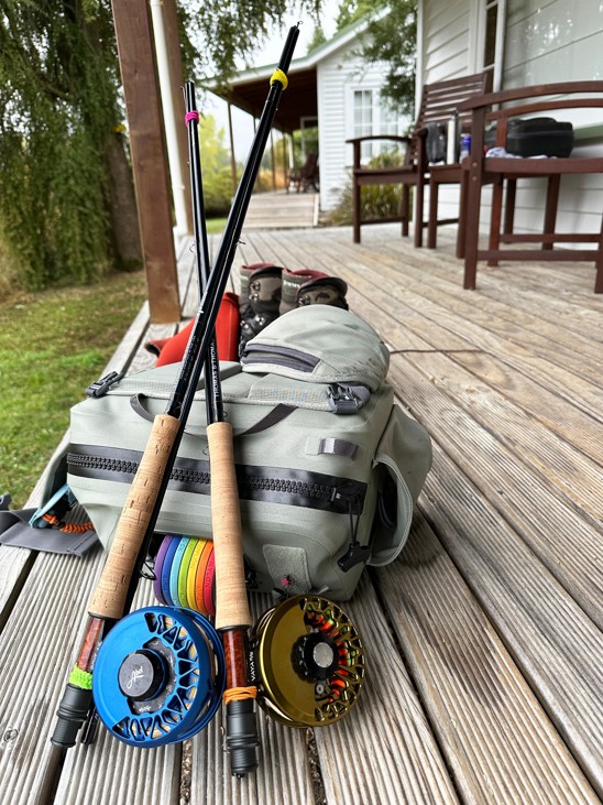 A close up of two fishing poles and reels and a back pack full of fishing equipment.
